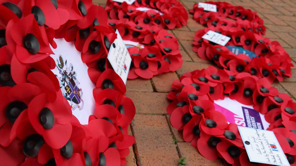 Poppy wreaths with the Loughborough University crest in the centre, laid on the ground with handwritten postcards.