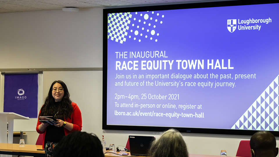 Photo of Dr Angela Martinez Dy speaking to the audience at the Race Equity Town Hall, with a screen behind her