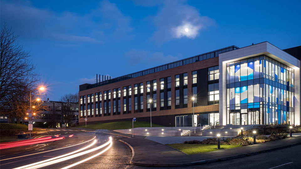 Photo of the exterior of STEMLab in the evening with lights from a vehicle driven at speed on view on the campus road