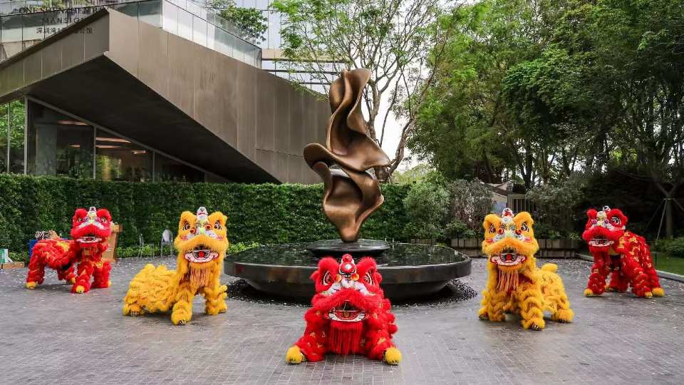 A bronze sculpture in the middle of a fountain surrounded by five red and yellow lion statues.