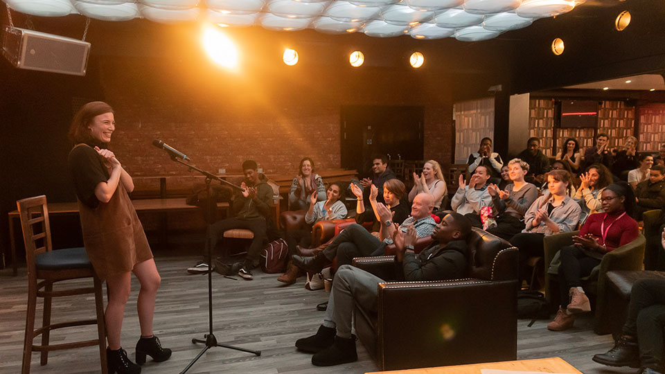 Photo of a performer on the stage in Cognitos, with a seated audience watching