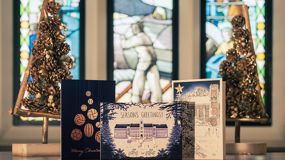 Photo of the three winning designs propped up on a table with stained glass window behind and two wooden Christmas trees on either side