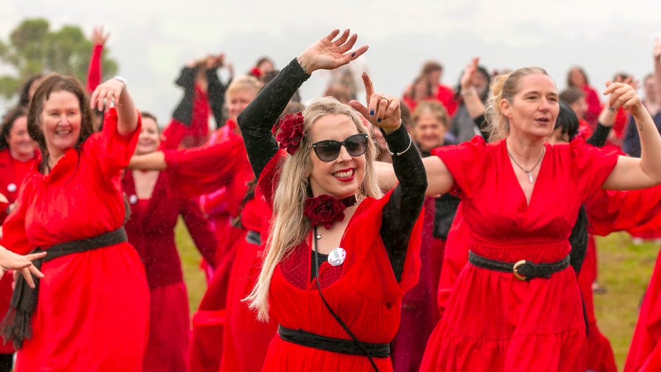 A group of people wearing red dresses, dancing together in a field.