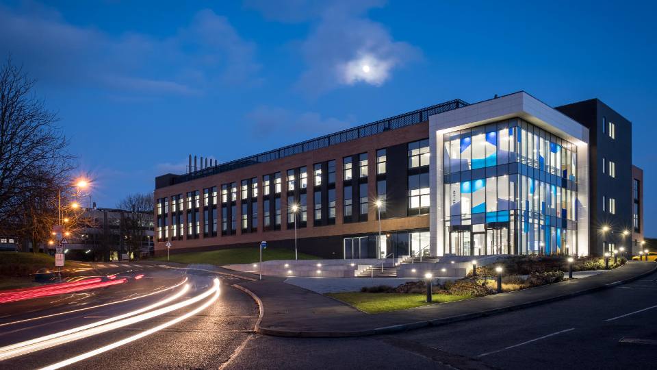 A dark evening with the STEMLab building lit up and a car light stretching along the road