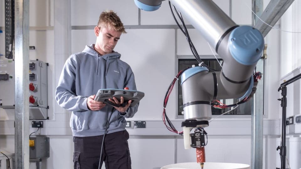 A student in a lab holding a tablet computer controling a robotic arm